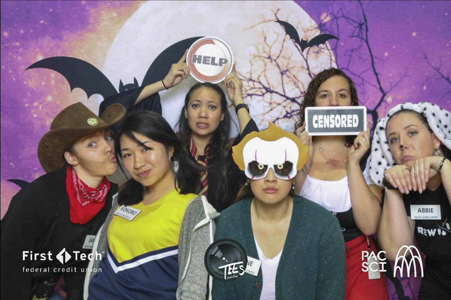 Group of guests holding Halloween props at corporate photo booth with bat backdrop