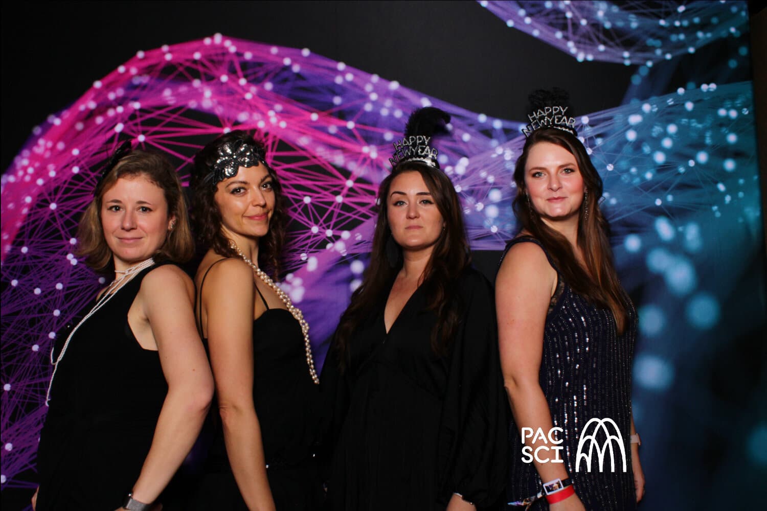 Four women wearing Happy New Year tiaras posing at vintage photo booth
