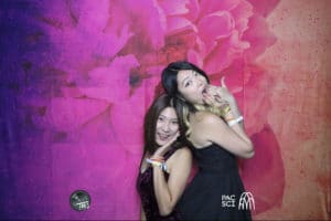 Two women posing close together at photo booth with red watercolor backdrop