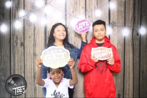 Family of three holding Love and message props at rustic wood photo booth