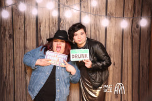 Two friends holding humorous Drunk and message props at rustic photo booth