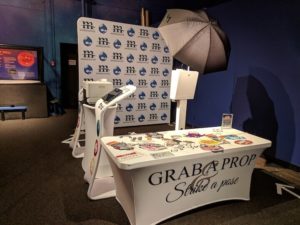 Photo booth with branded M&M backdrop, prop table and umbrella light at venue