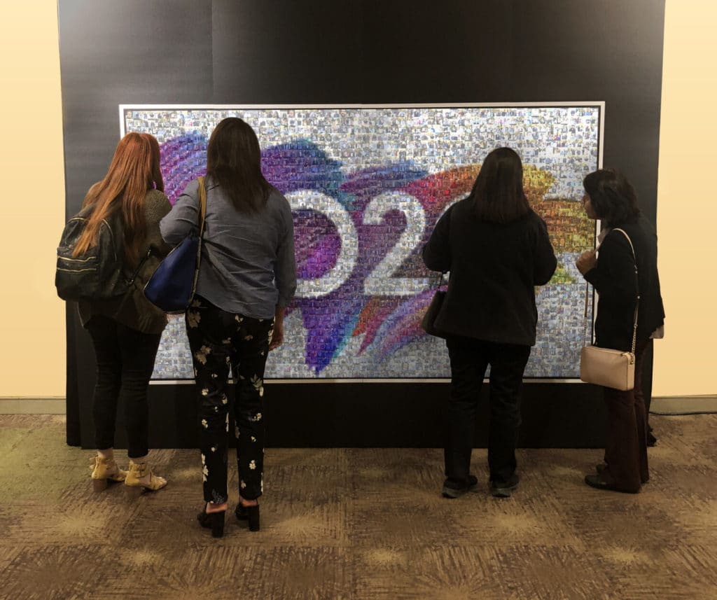 Four women viewing colorful Wall Mosaic photo collage display in corporate lobby