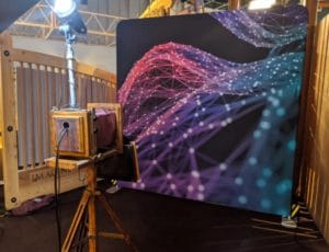 Vintage wooden camera booth facing purple geometric mesh backdrop at venue