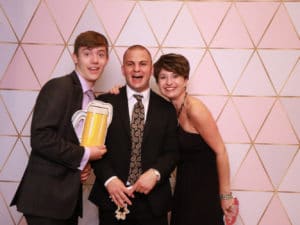 Three friends posing with beer mug prop at pink geometric photo booth backdrop