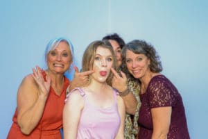 Group of women making playful faces at photo booth on light blue backdrop