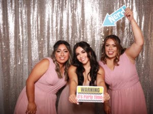 Three women holding playful sign props at silver sequin photo booth backdrop