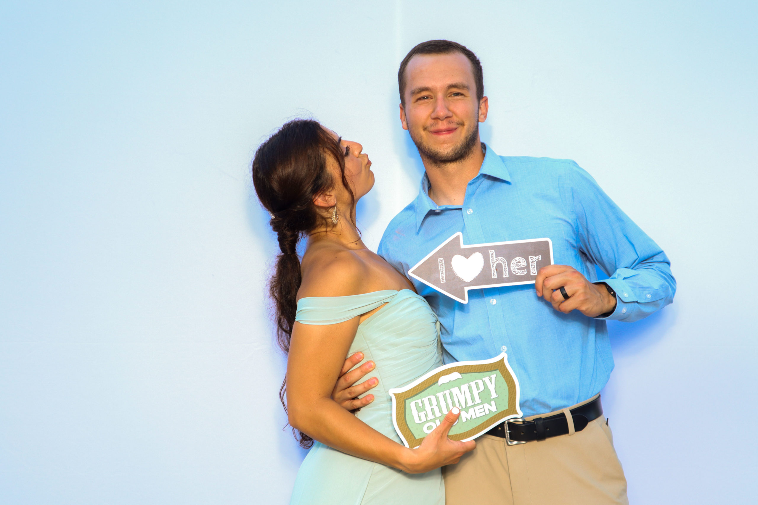 Couple holding I love her and Grumpy Old Men props at photo booth