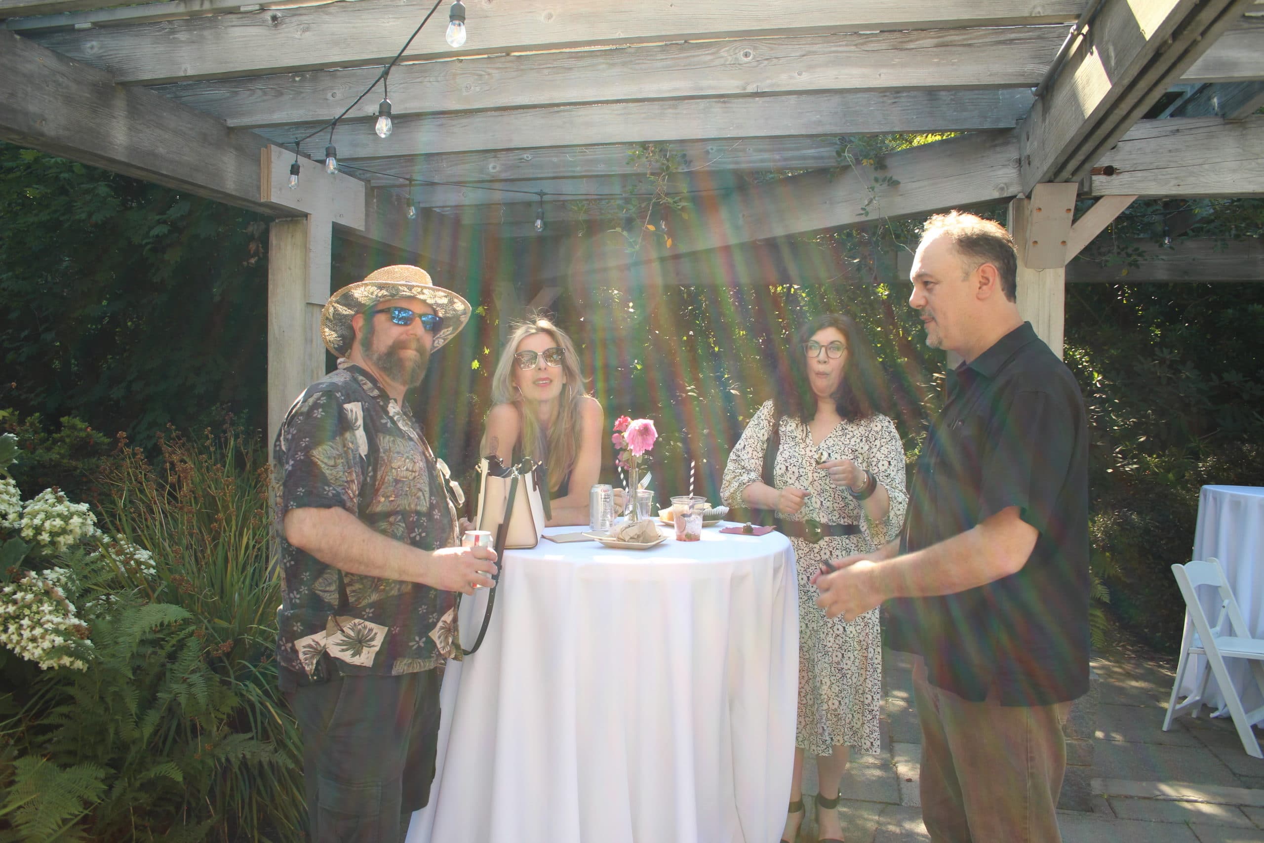 Group of friends in casual attire chatting around table at sunny outdoor garden party