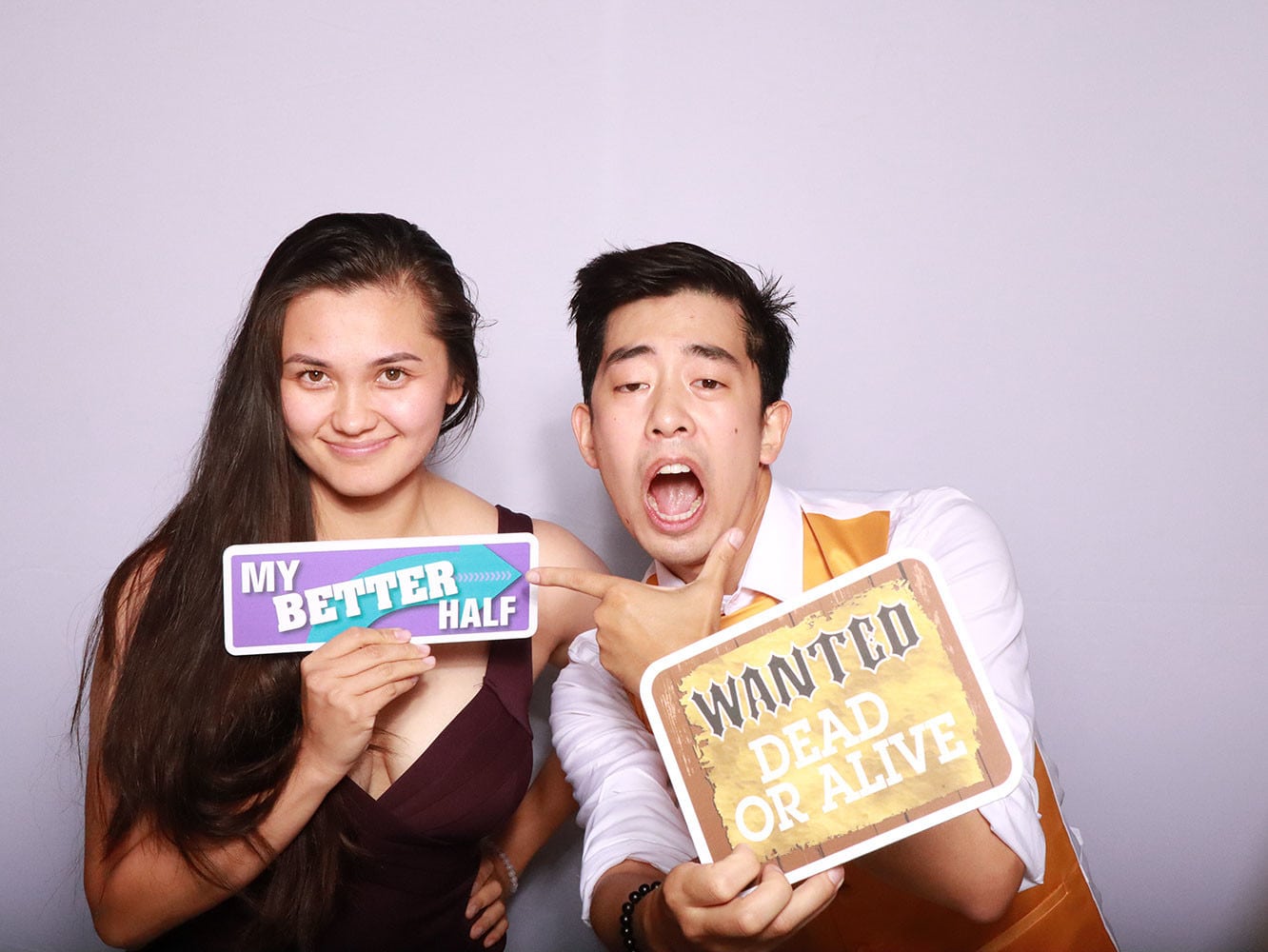 Couple holding My Better Half and Wanted Dead or Alive sign props at photo booth