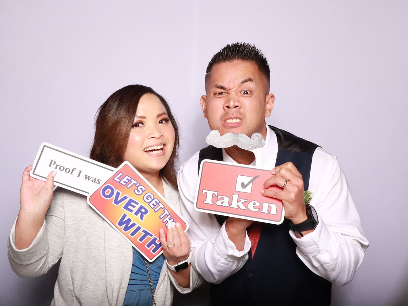Couple making playful expressions with mustache and Taken sign props at booth