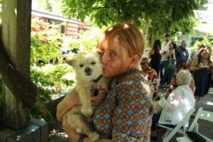Woman holding small white dog at outdoor garden gathering