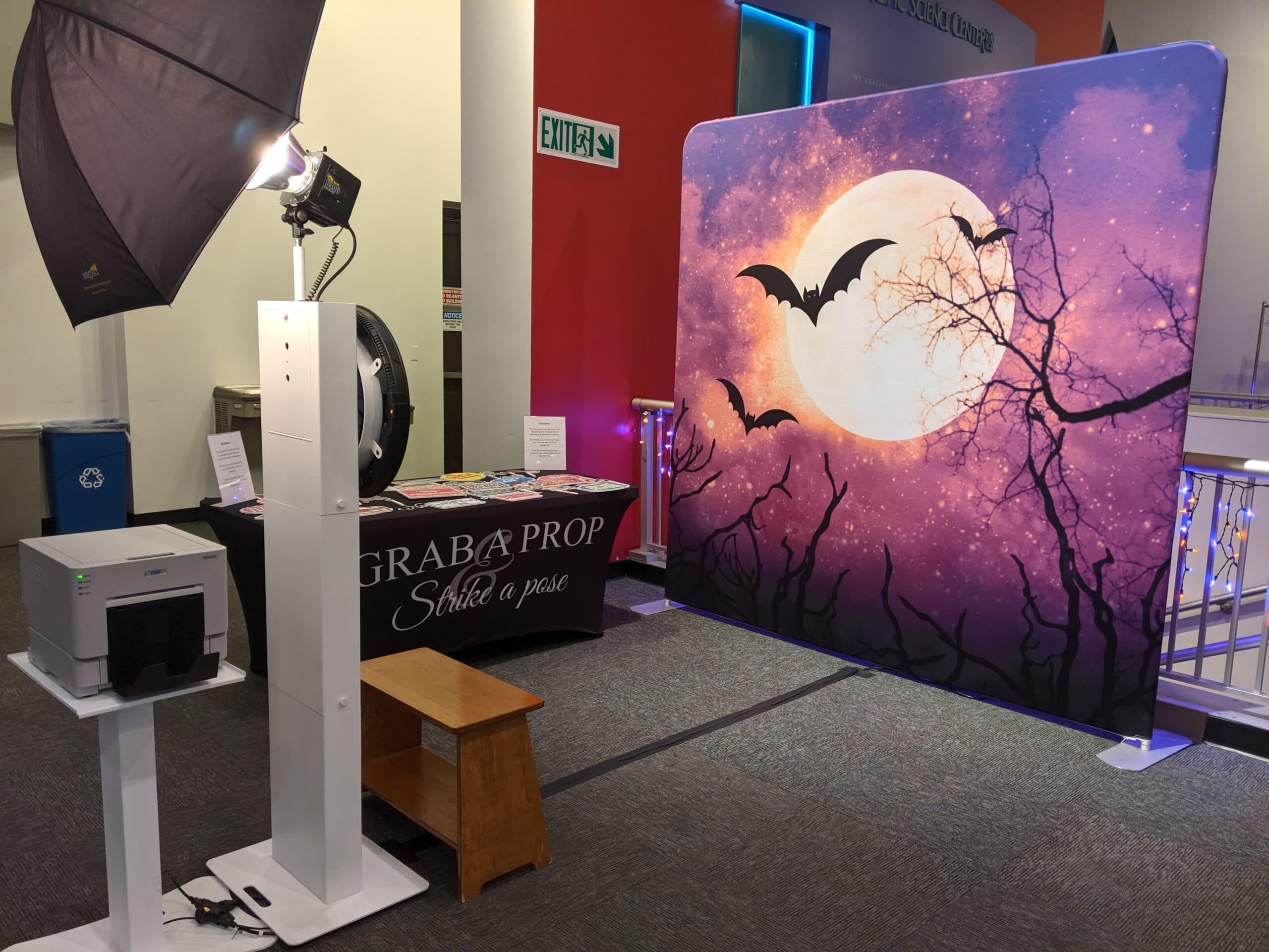 Photo booth with purple Halloween moon and bats backdrop and prop table