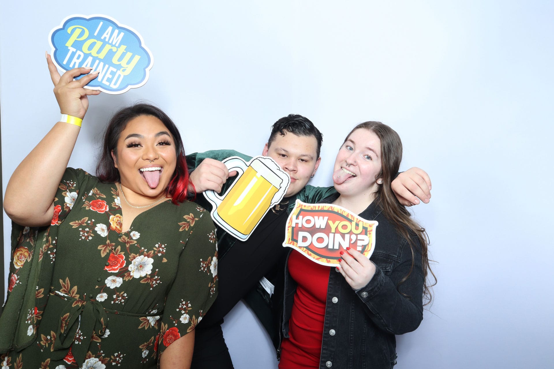 Three friends holding I Am Party Trained beer mug and How You Doin props at booth