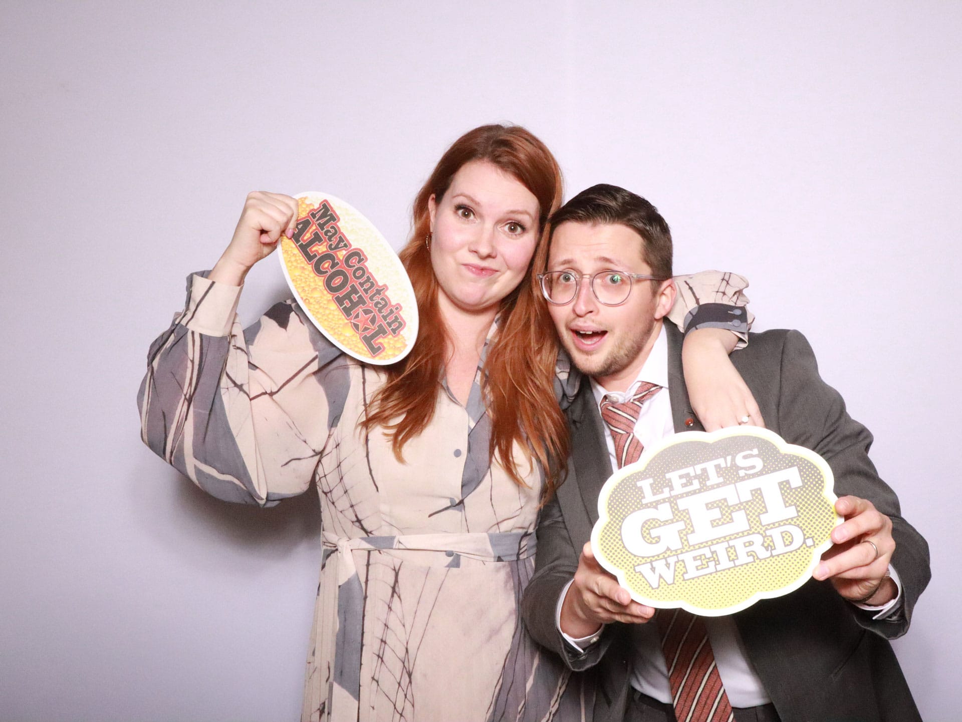 Couple holding Mr and Mrs and Lets Get Weird sign props at lavender backdrop