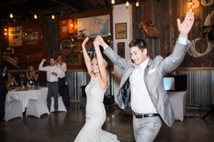 Bride and groom dancing with arms raised at rustic industrial wedding venue