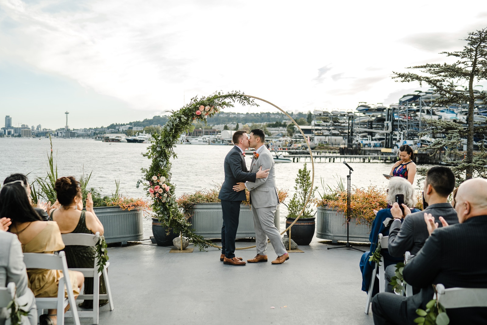 Two grooms kissing at outdoor waterfront wedding ceremony with Seattle Space Needle view