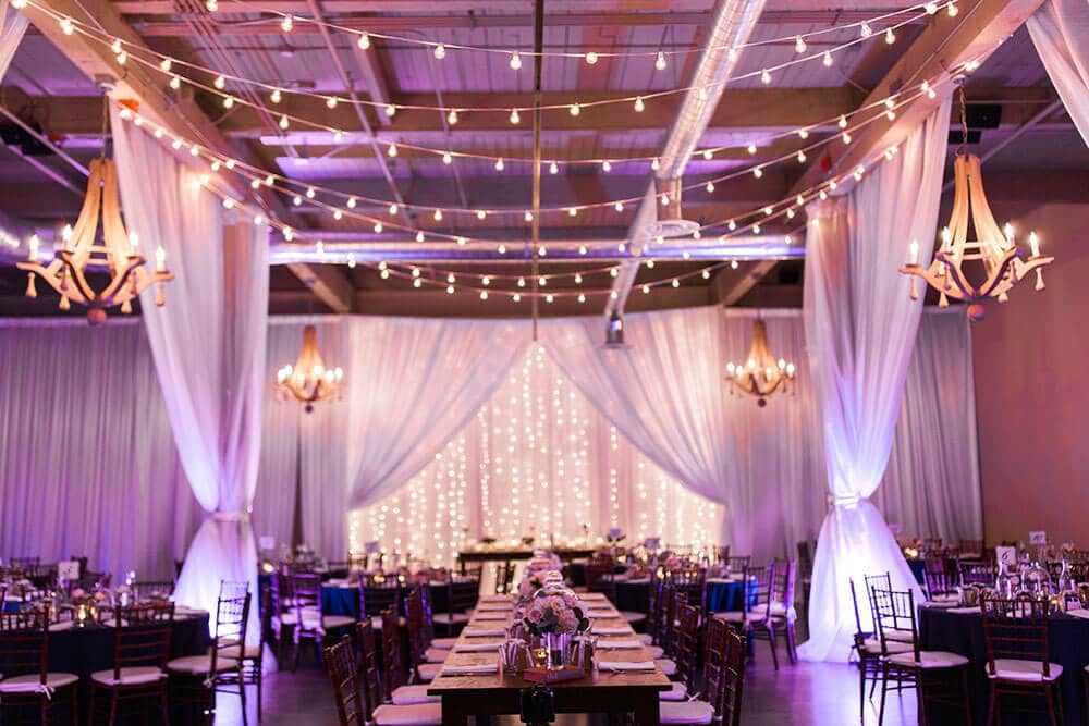 Foundry wedding venue with white draping, chandeliers and string light ceiling
