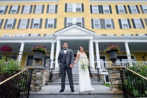 Bride and groom posing on porch steps of yellow Mountain View Grand hotel