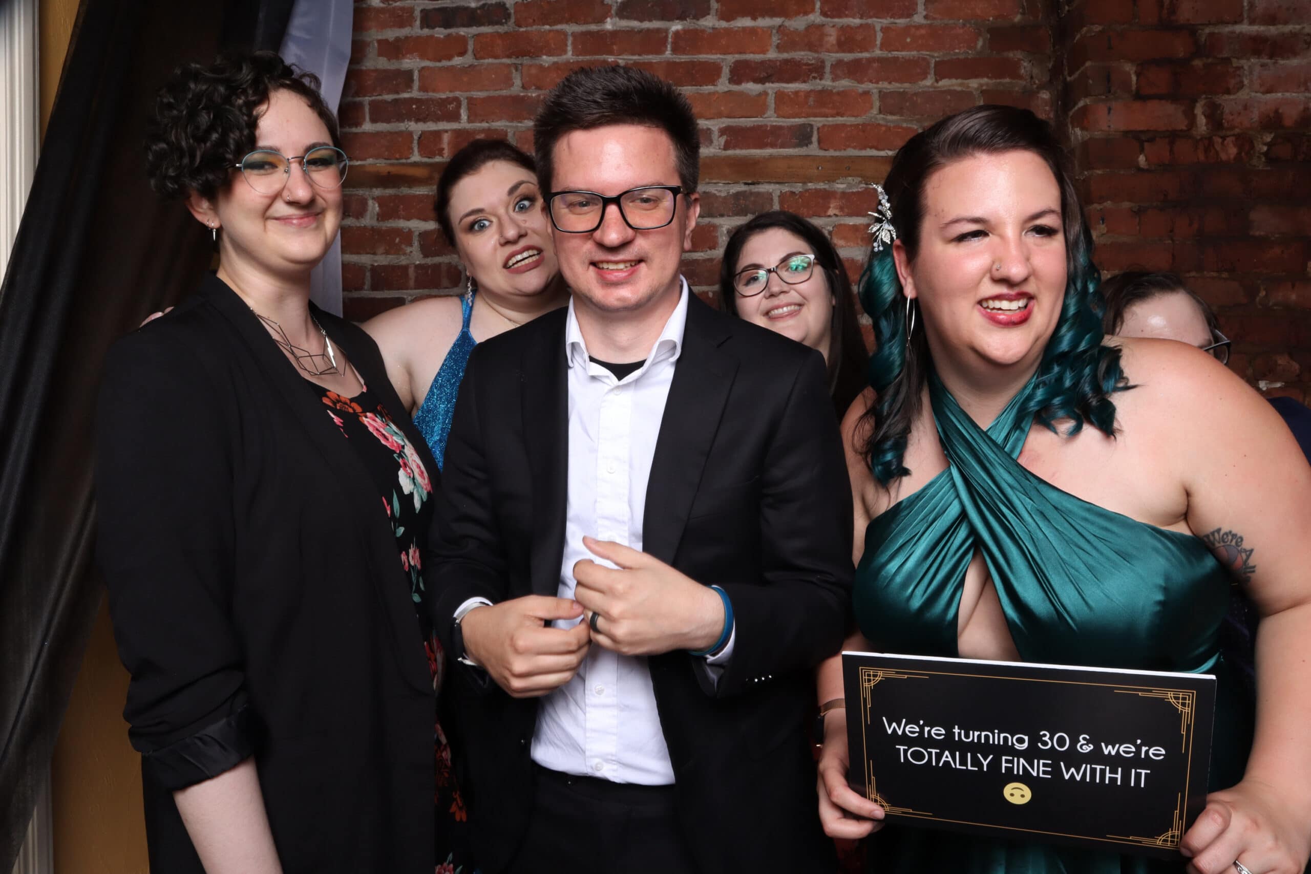 Group celebrating birthday milestone holding sign at brick wall photo booth