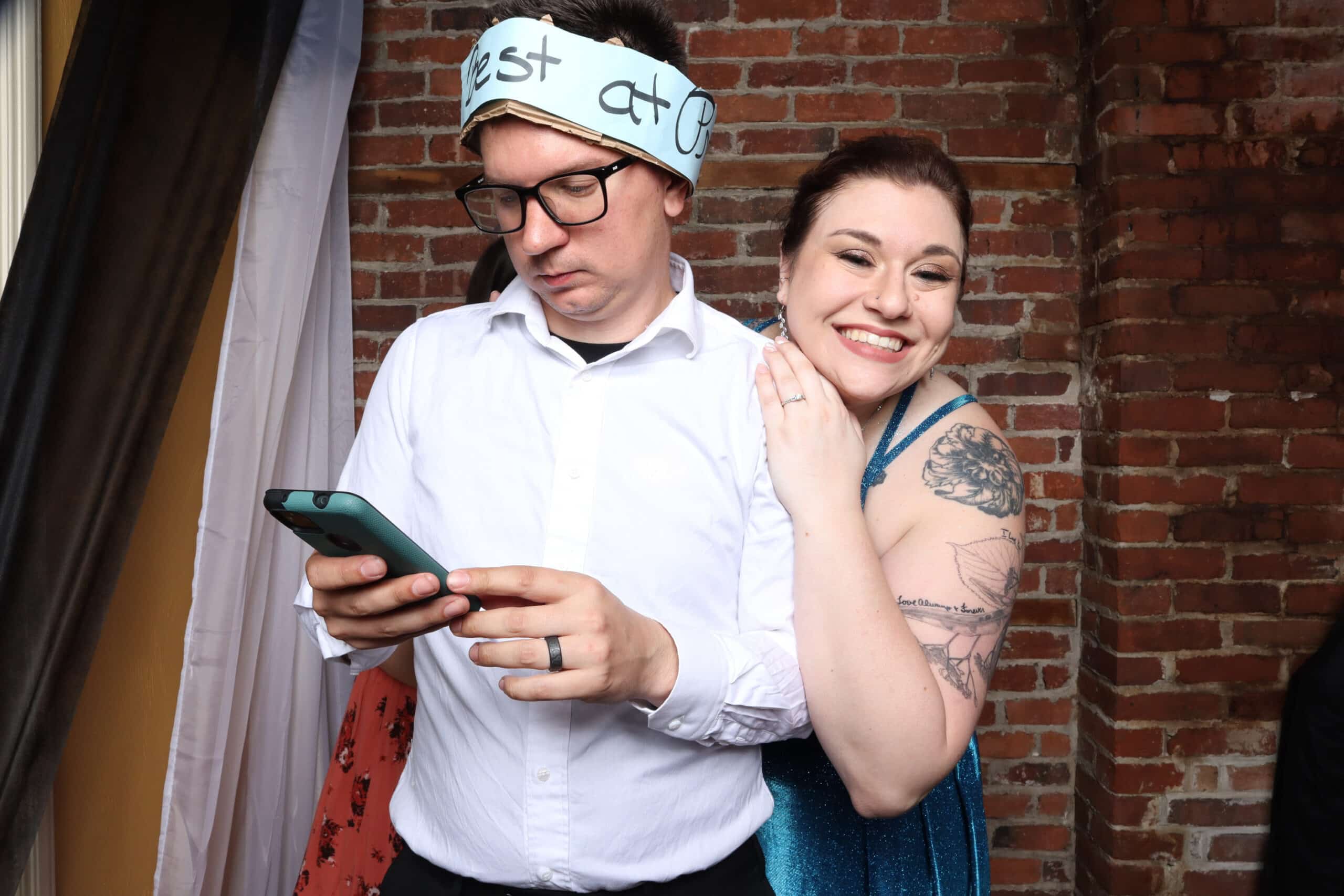 Couple posing playfully against brick wall backdrop with phone and headband