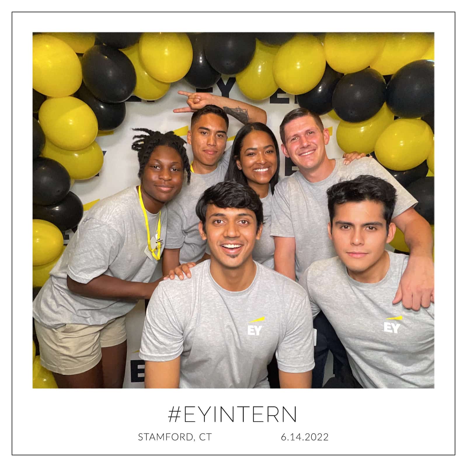 Group of EY interns posing at corporate photo booth with yellow and black balloons