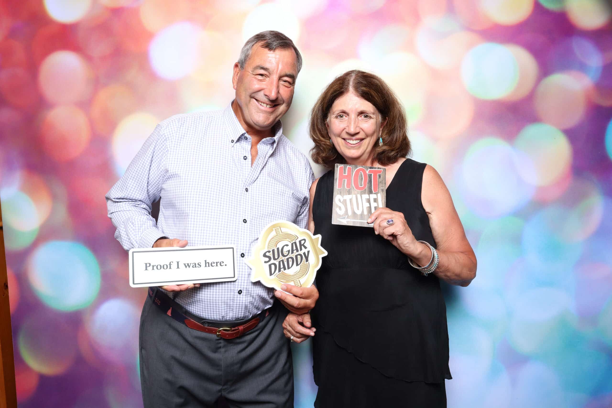 Couple holding Proof I was here, Sugar Daddy and Hot Stuff sign props at booth