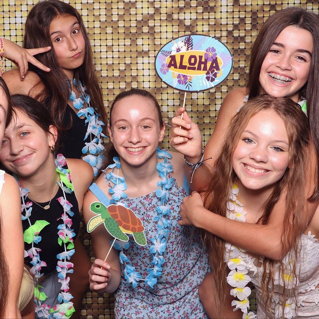 Group of teens holding Aloha sign and turtle props at gold sequin photo booth