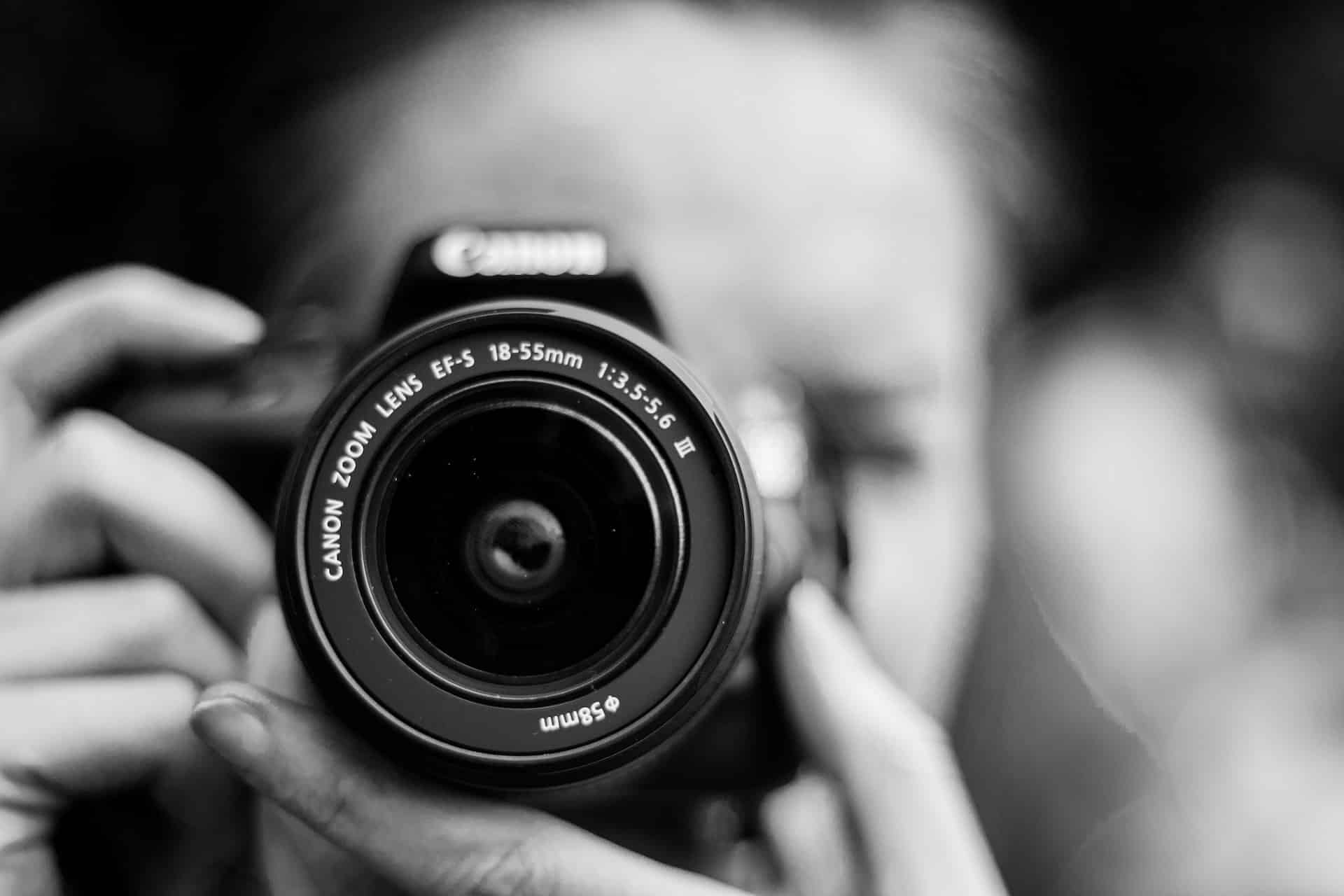 Black and white photo of person looking through DSLR camera viewfinder