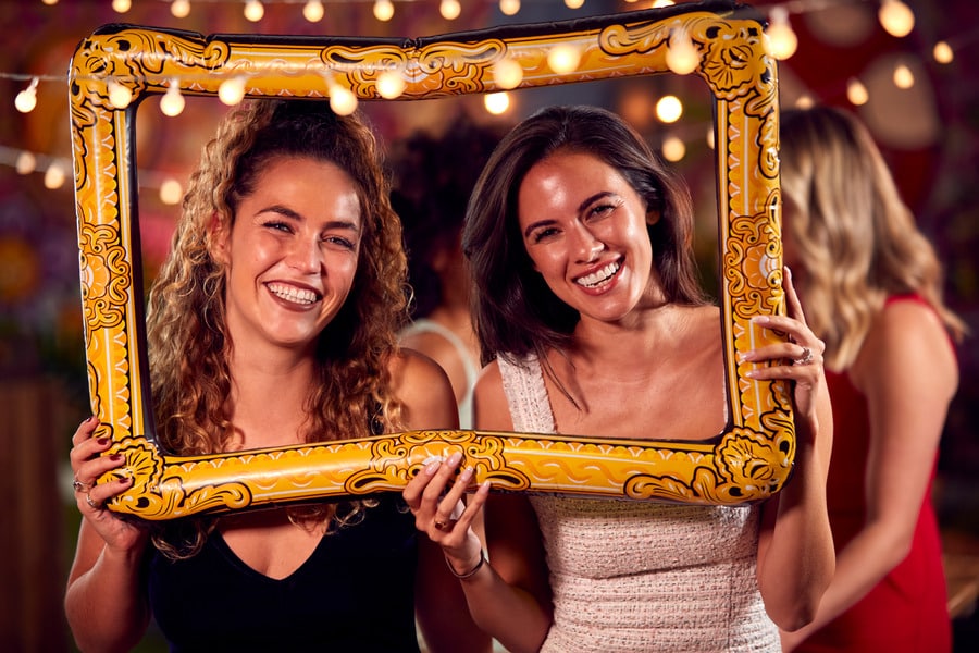 Two friends smiling through ornate gold picture frame prop at party