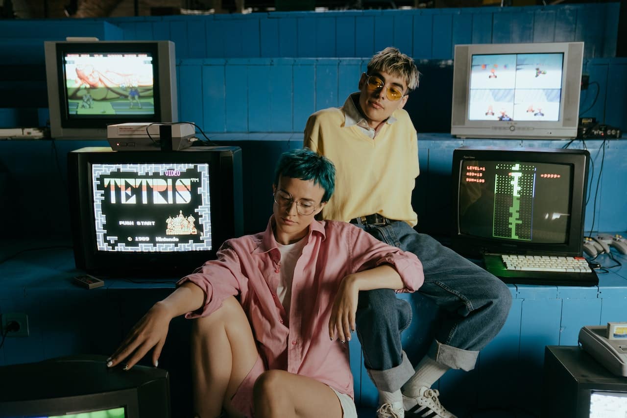 Two friends posing playfully with retro CRT TVs displaying classic video games