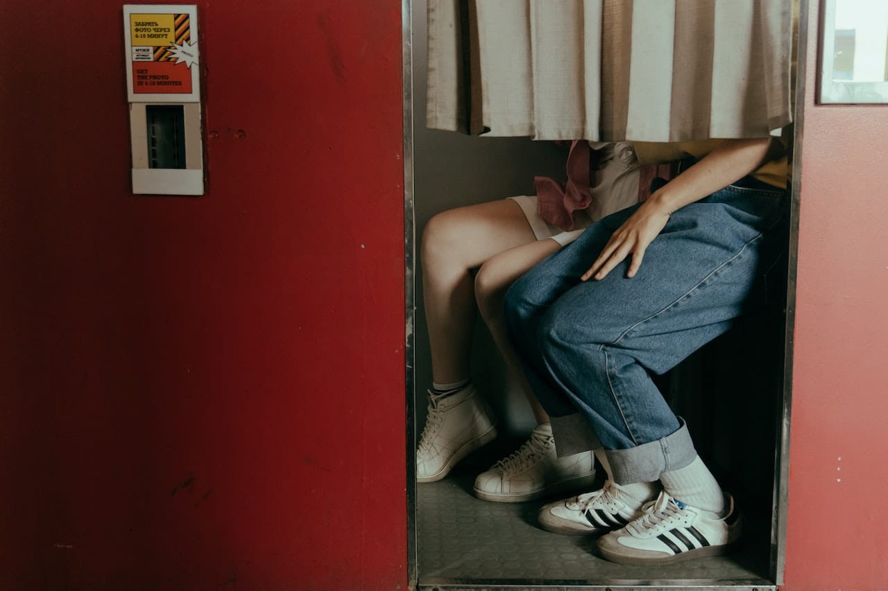 Person sitting inside vintage red photo booth visible through curtained doorway