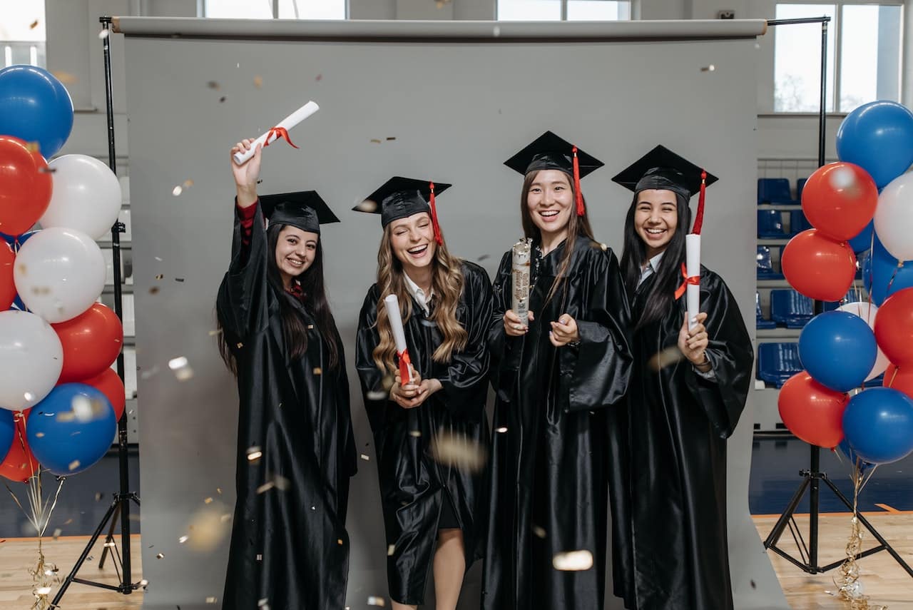 Group of graduates in caps and gowns celebrating with diplomas and balloons