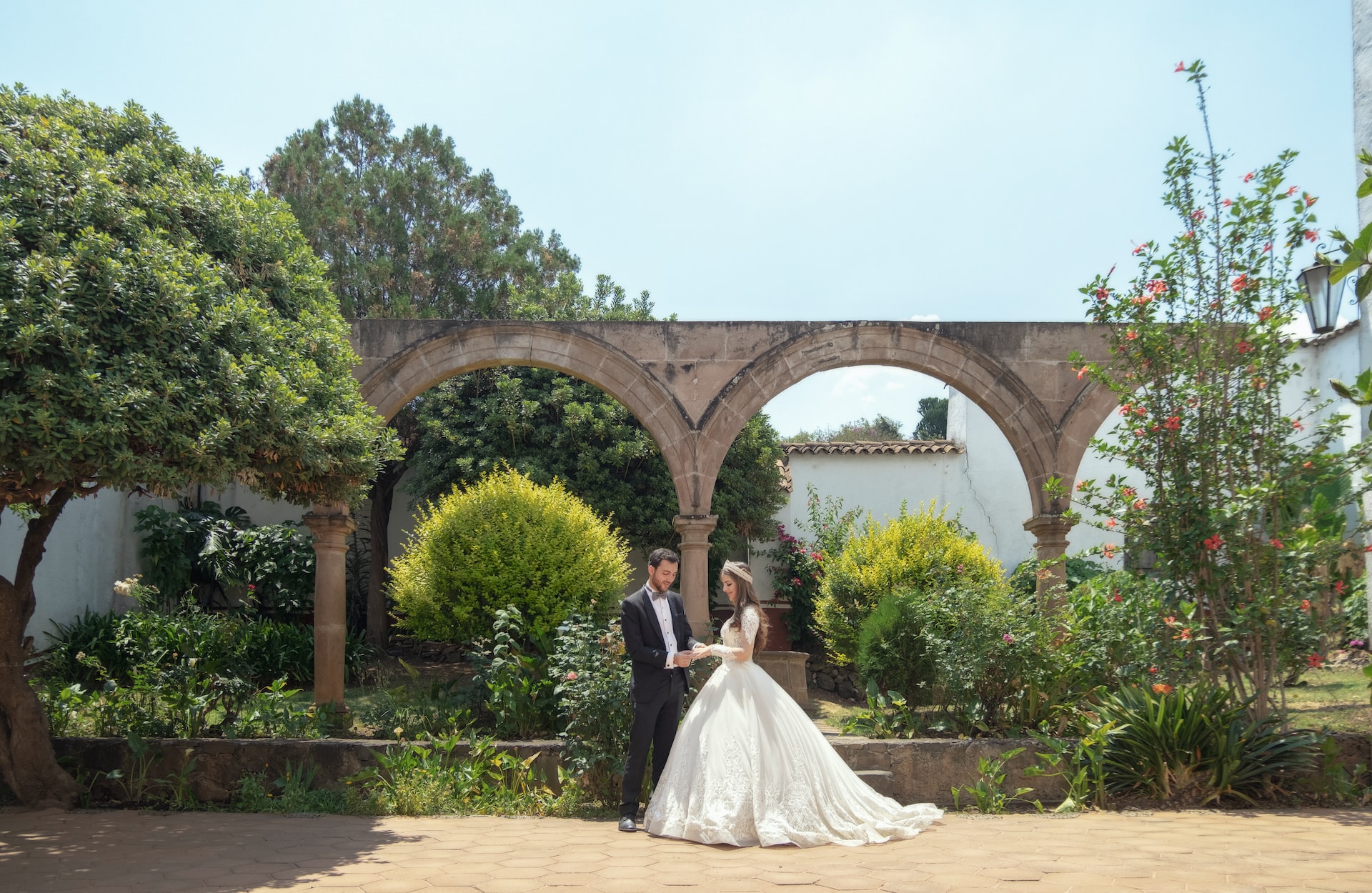 Bride and groom posing at stone arch garden venue on sunny day
