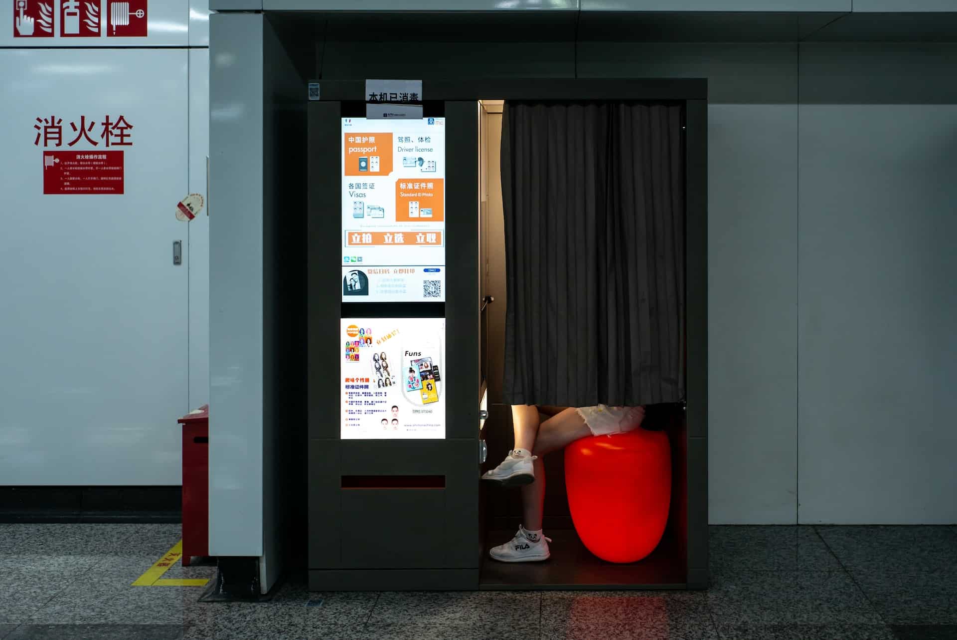 Vintage style photo booth with curtained doorway and red stool inside transit station
