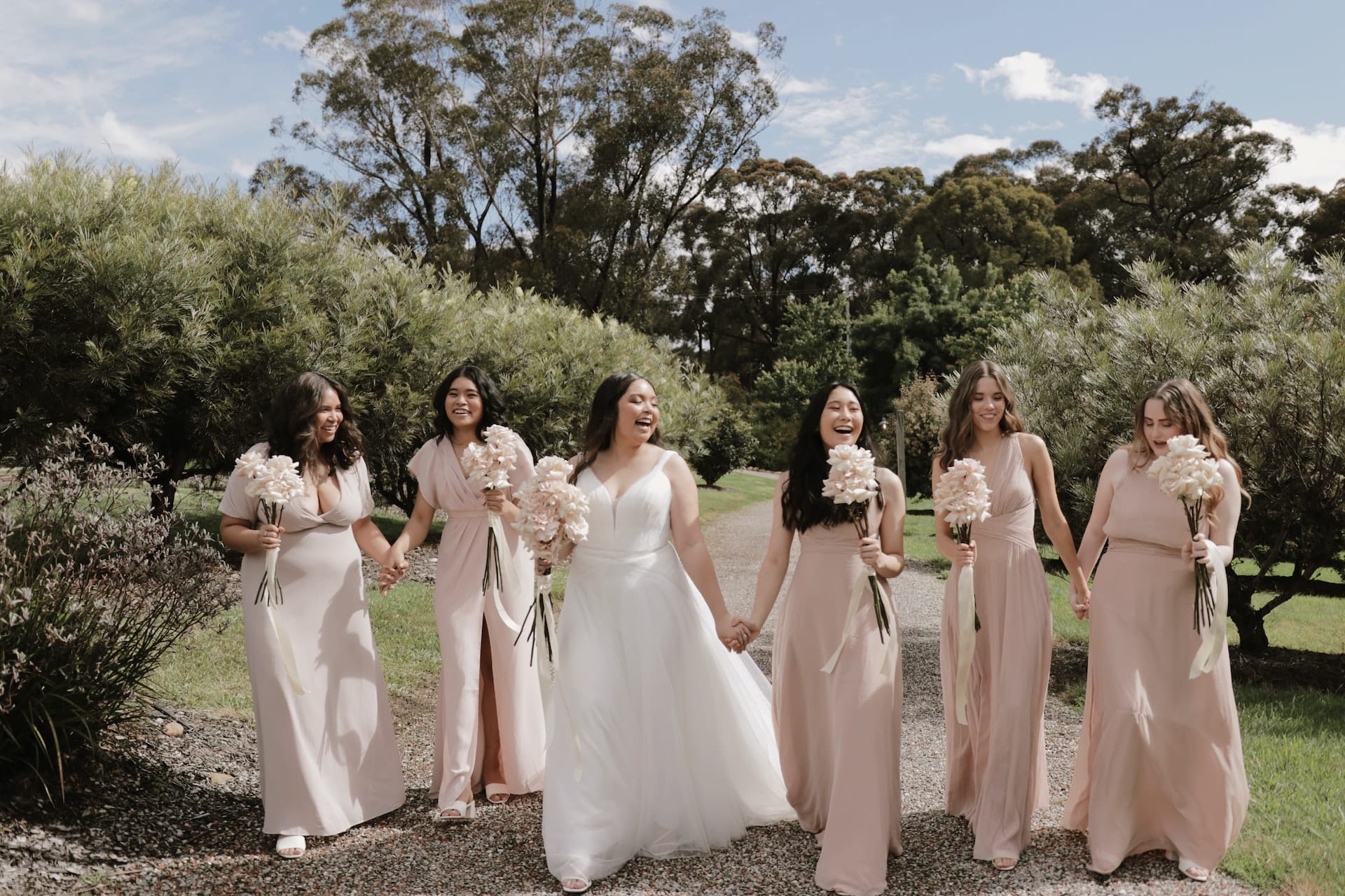 Bride and bridesmaids in blush gowns walking together at outdoor wedding