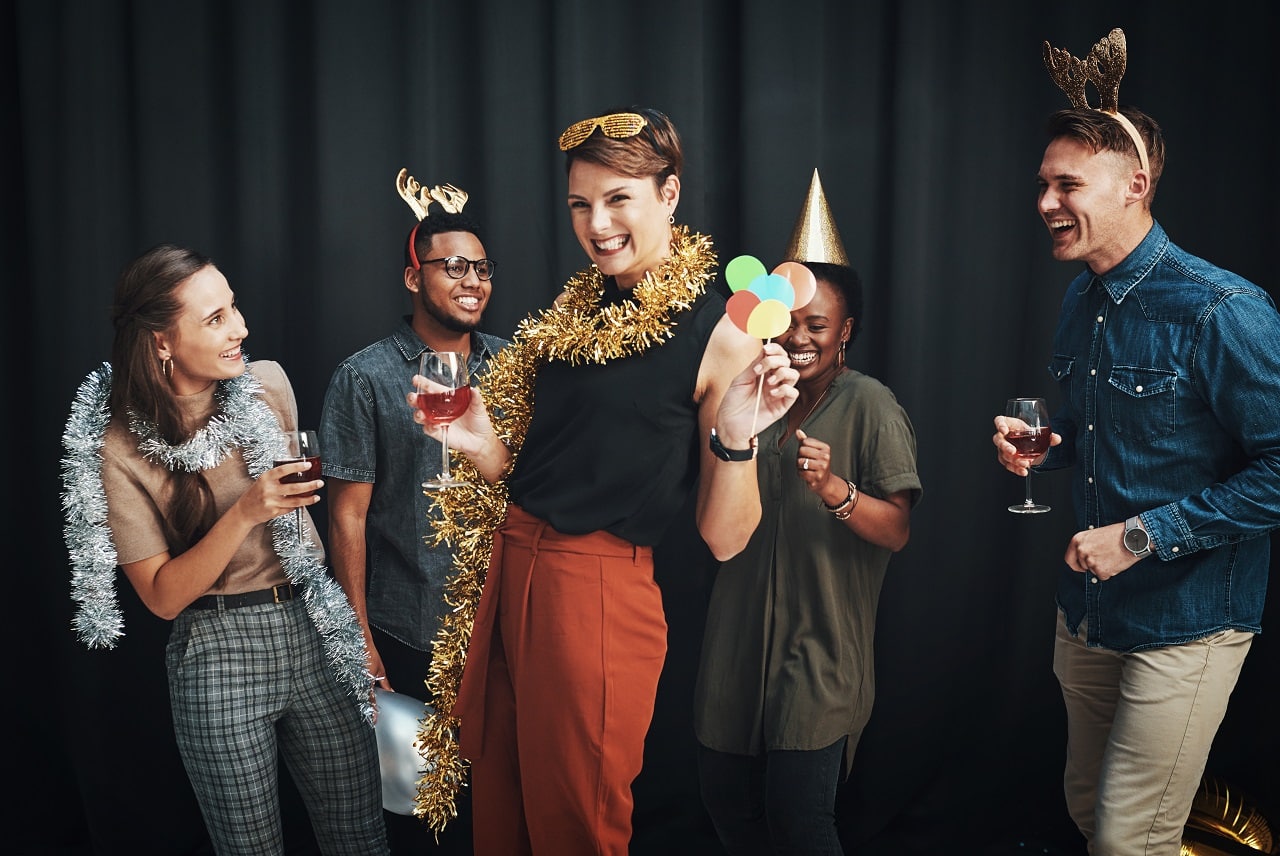 Group of friends in holiday tinsel and party hats laughing at photo booth