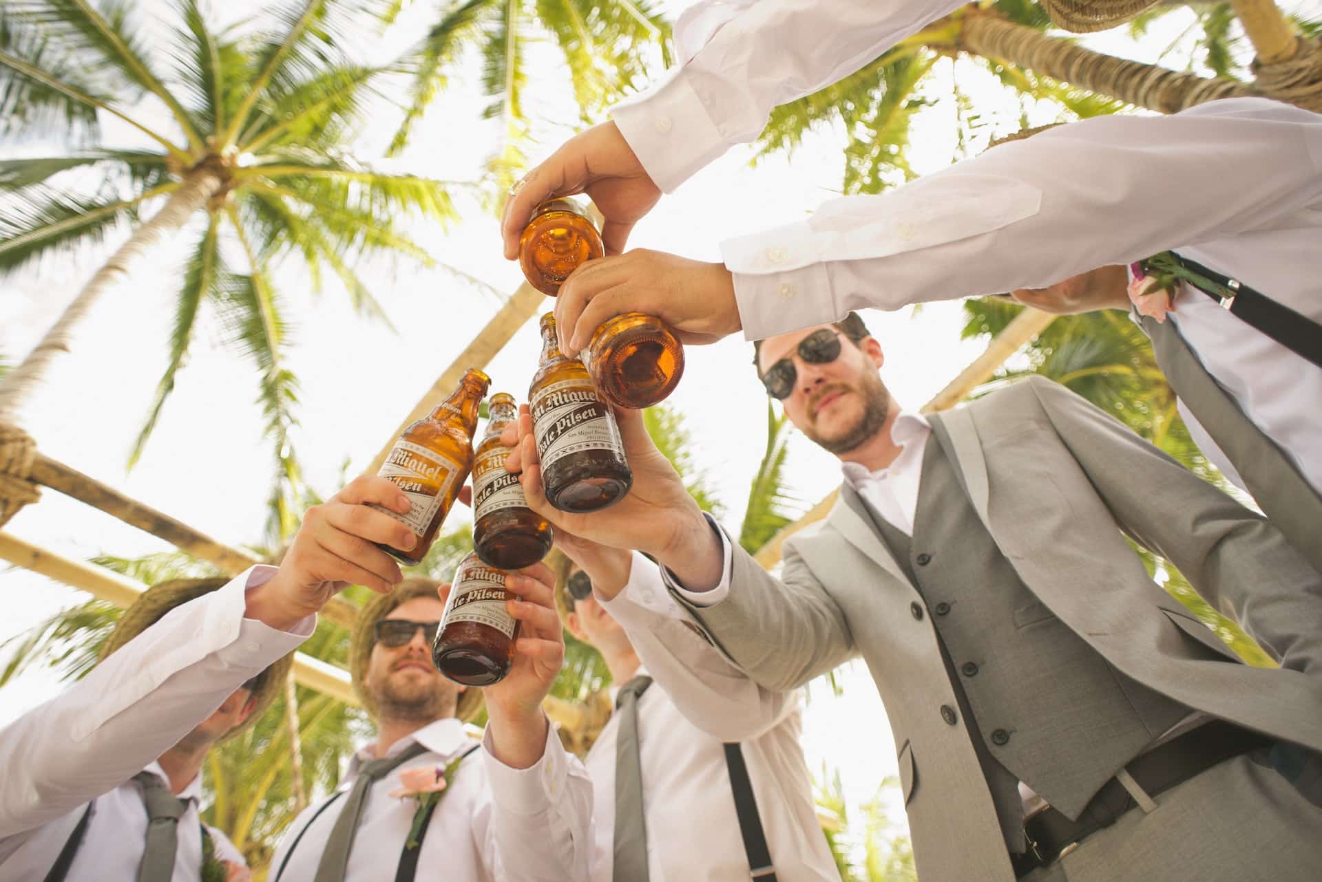 Groomsmen toasting beer bottles together at tropical destination wedding