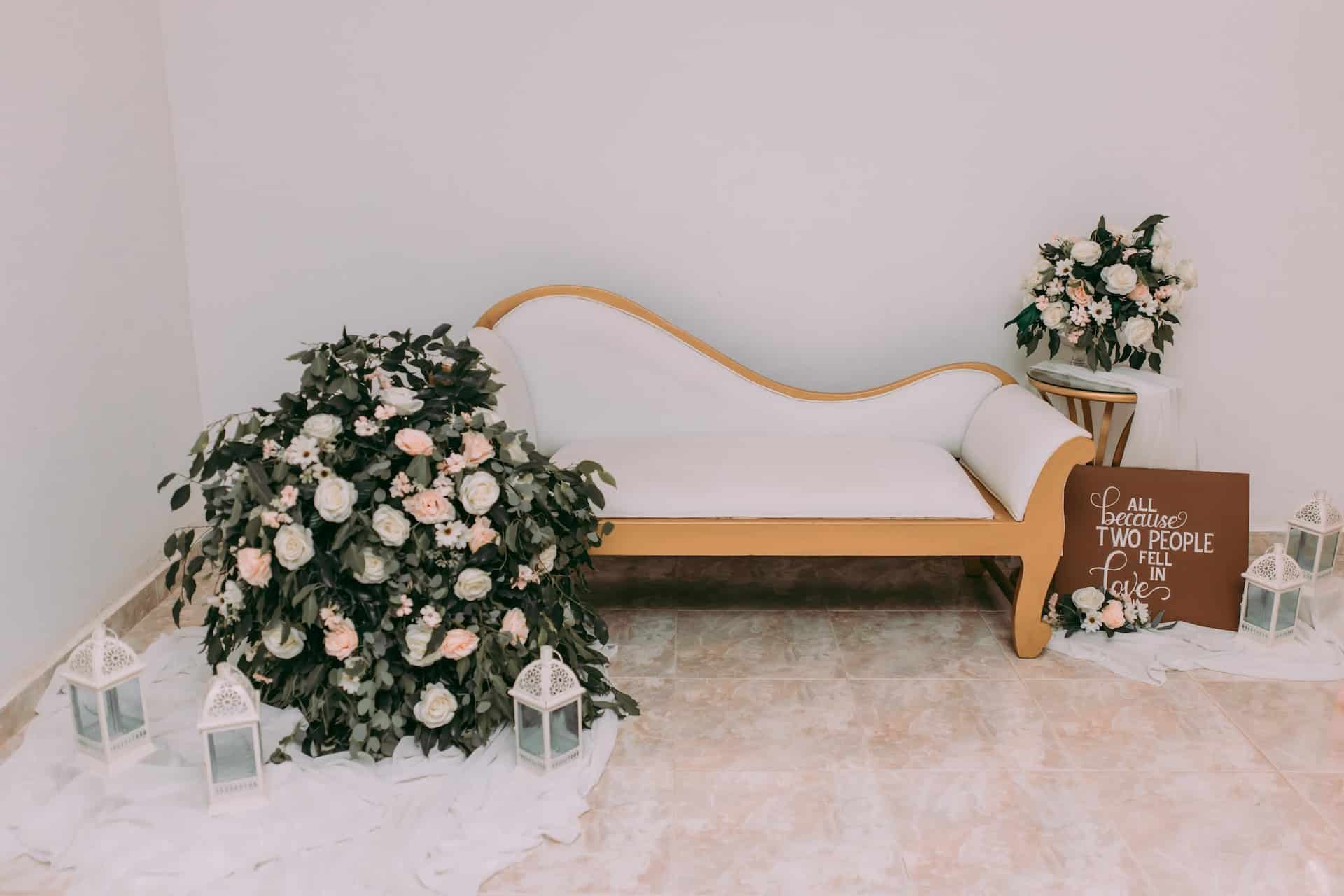 White chaise lounge with floral arrangements at minimalist wedding photo booth setup