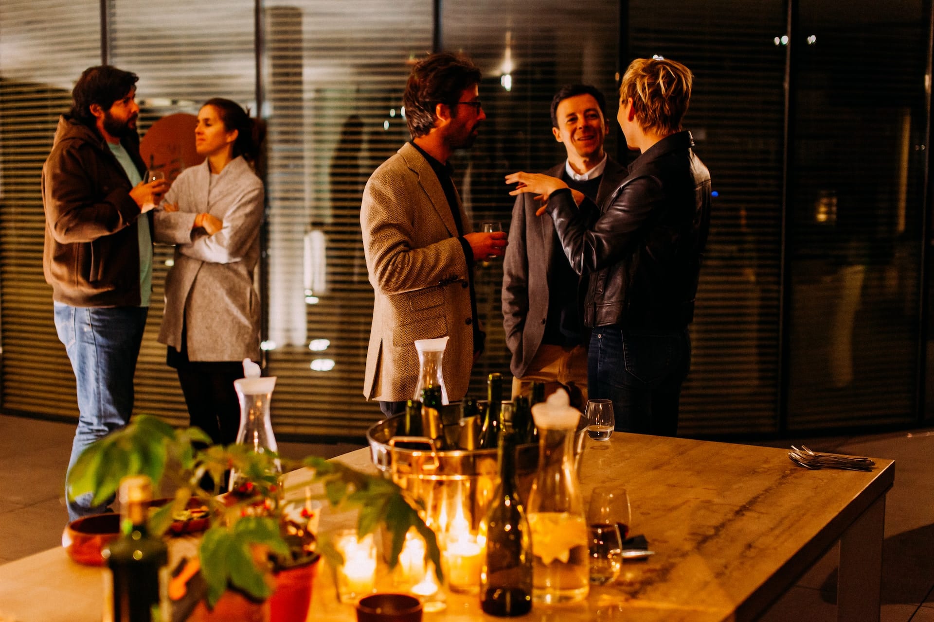 Group mingling at corporate cocktail event with candlelit table and wine bottles