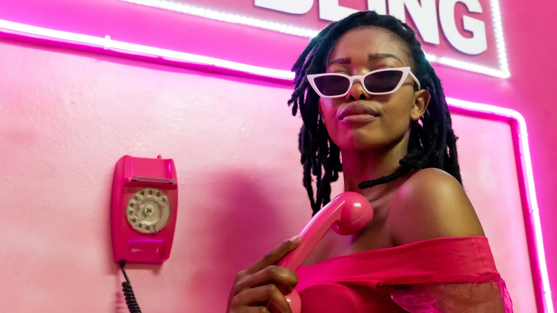 Woman posing with sunglasses near pink phone at bright pink photo set
