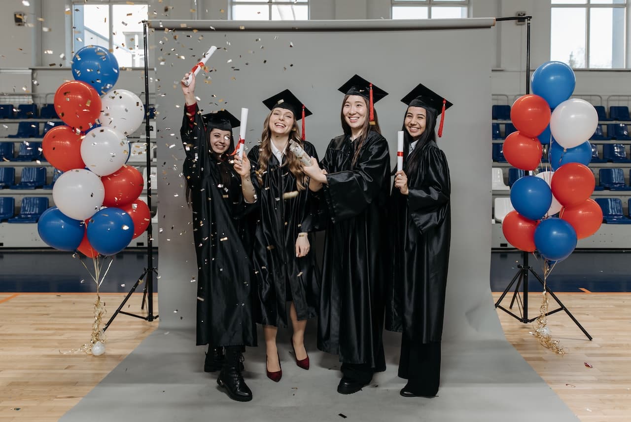 Group of female graduates celebrating with diplomas, confetti and balloon arches