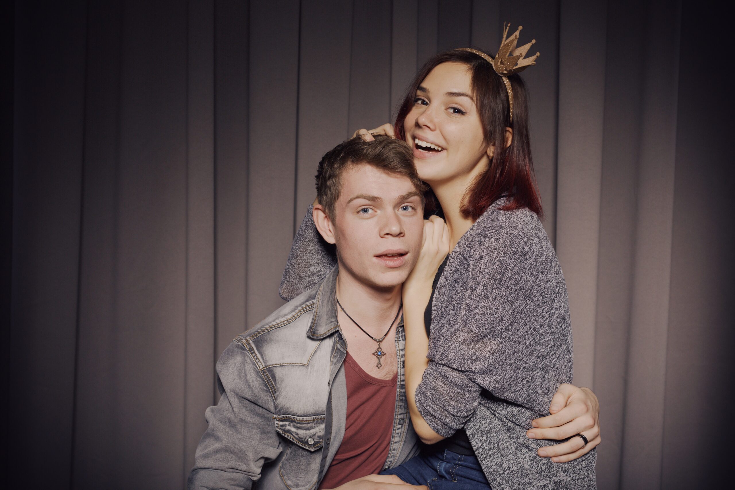 Young couple embracing playfully at curtained photo booth with warm lighting
