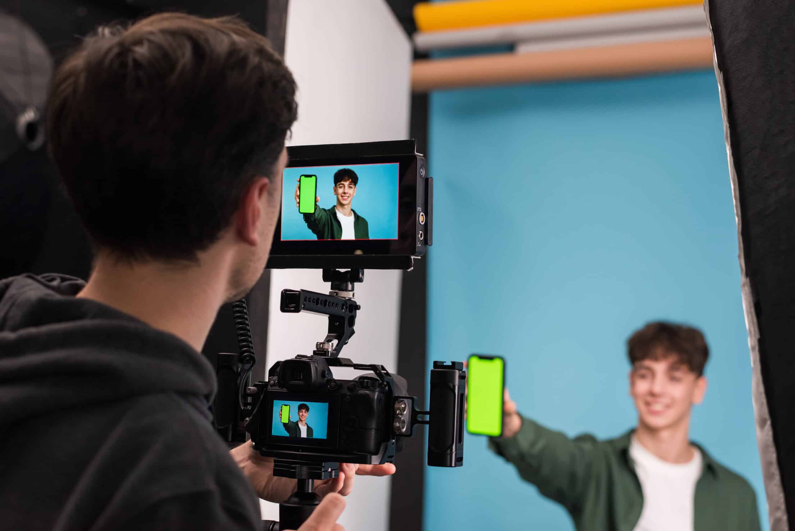 Photographer shooting young man against teal backdrop in studio setting