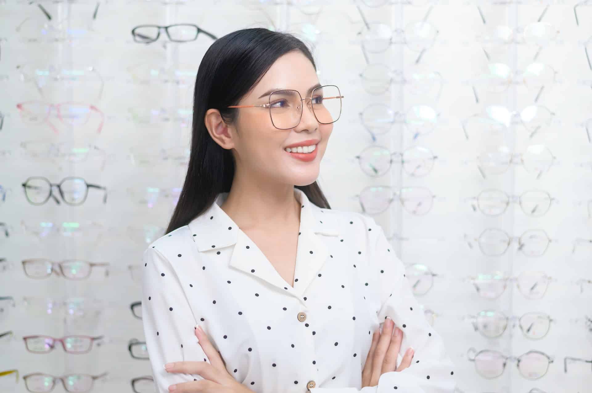 Woman in glasses smiling at optical store with eyewear displays behind her
