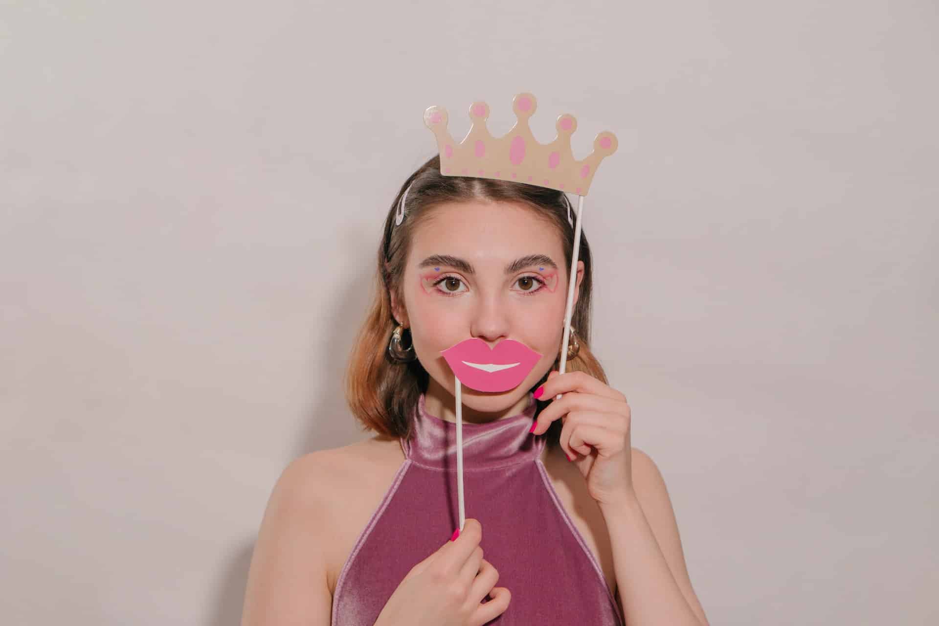 Woman holding paper crown and lips props at white photo booth backdrop