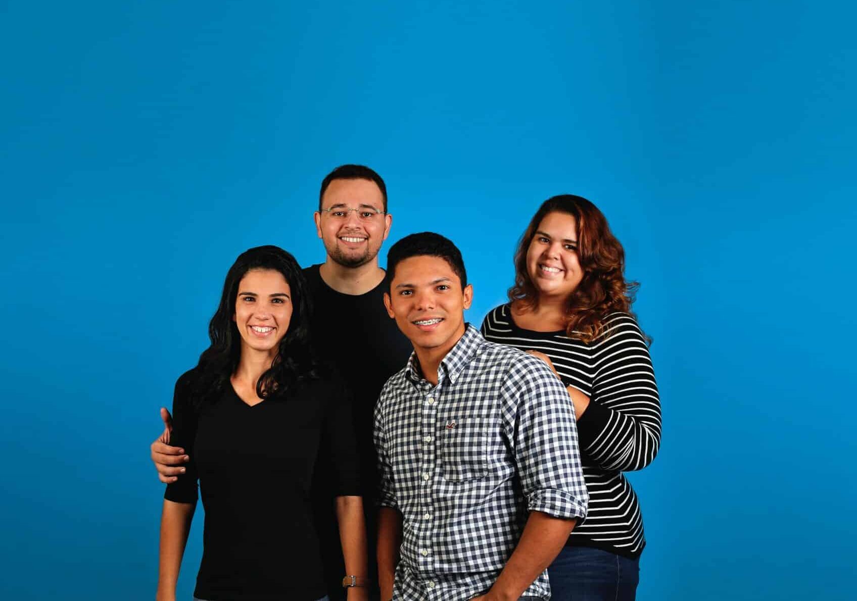 Family group of four smiling together against bright blue backdrop