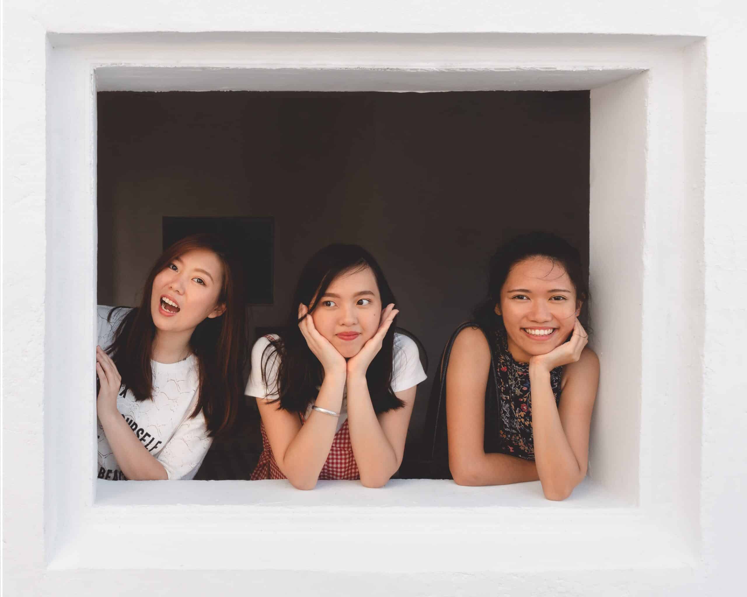 Three young women resting chins on hands inside white frame display
