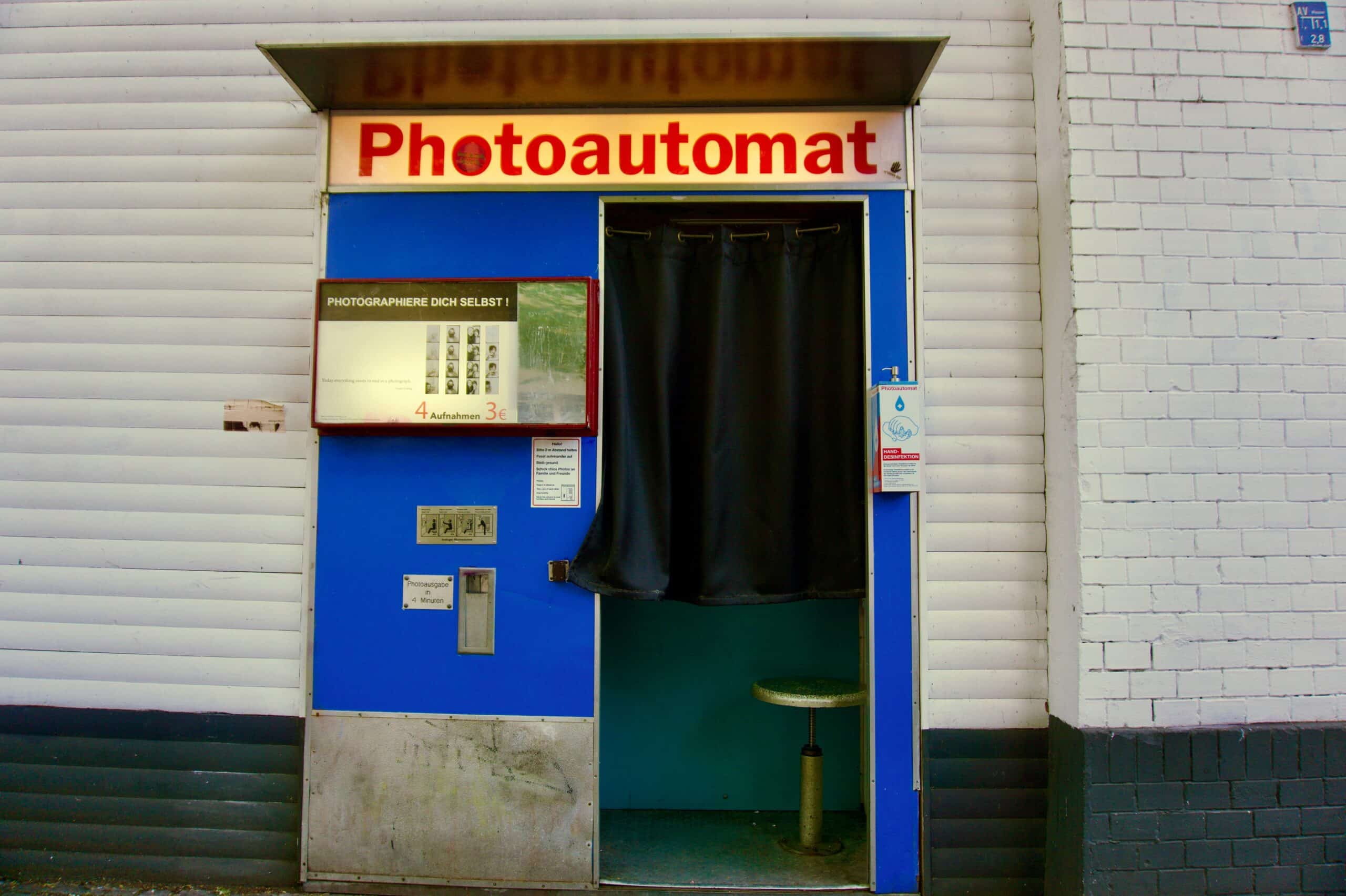 Vintage blue Photoautomat photo booth with curtained doorway on brick wall