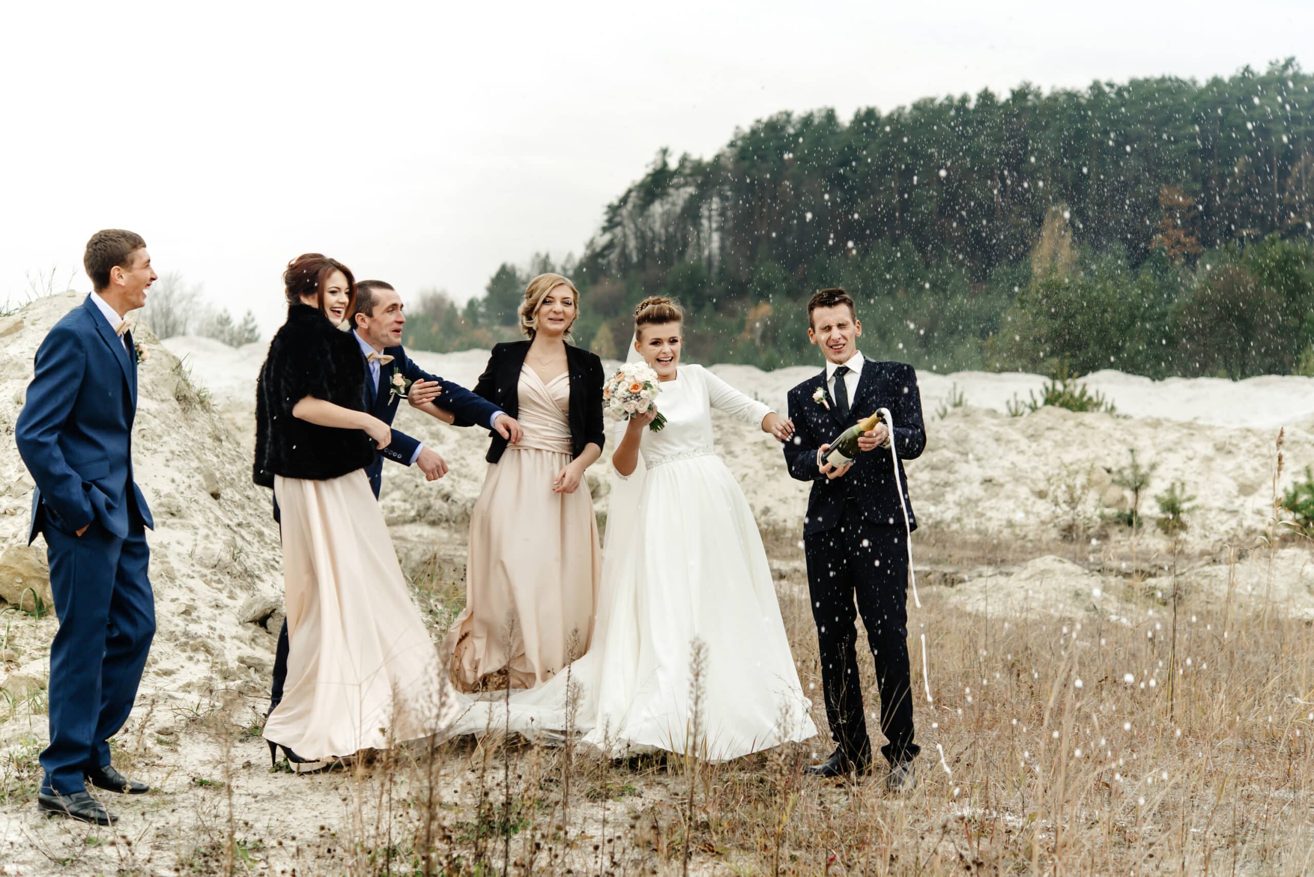 Bride and groom with wedding party drinking champagne in sandy outdoor setting